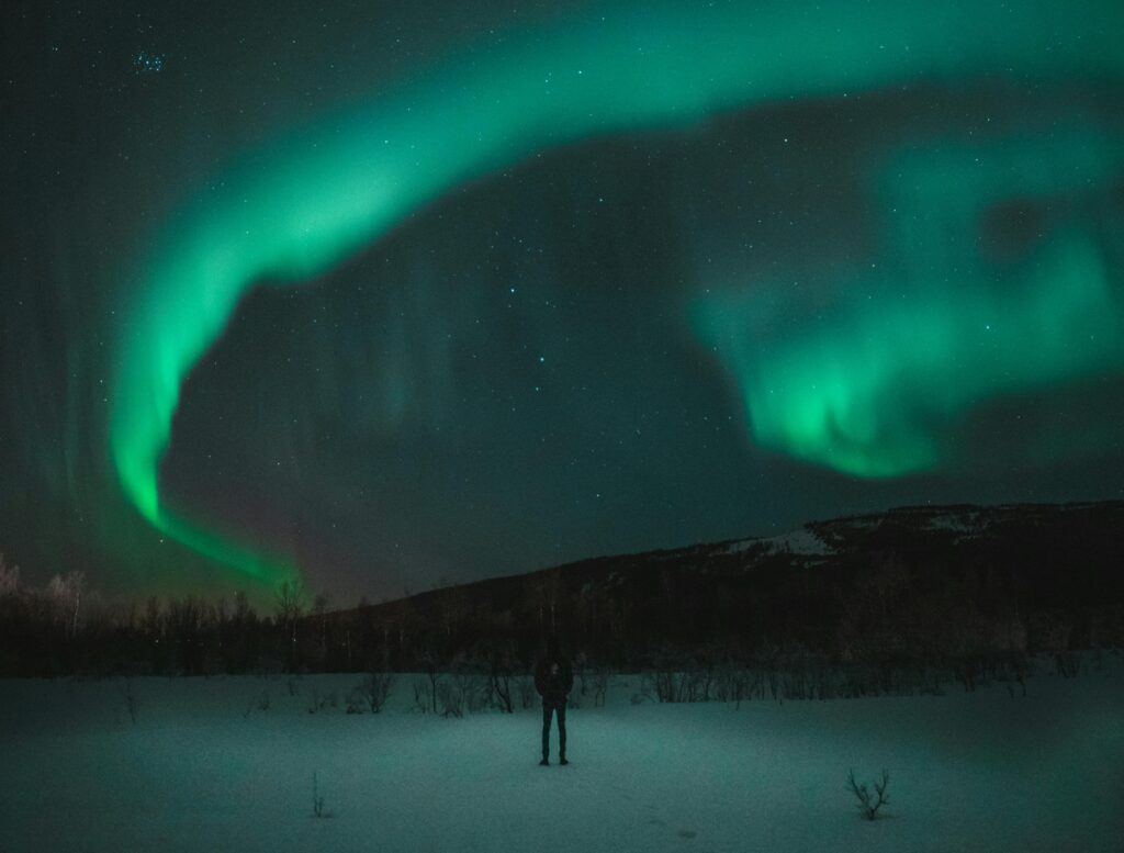 A mesmerizing display of the aurora borealis illuminating a snowy landscape with a person admiring the starry night sky.